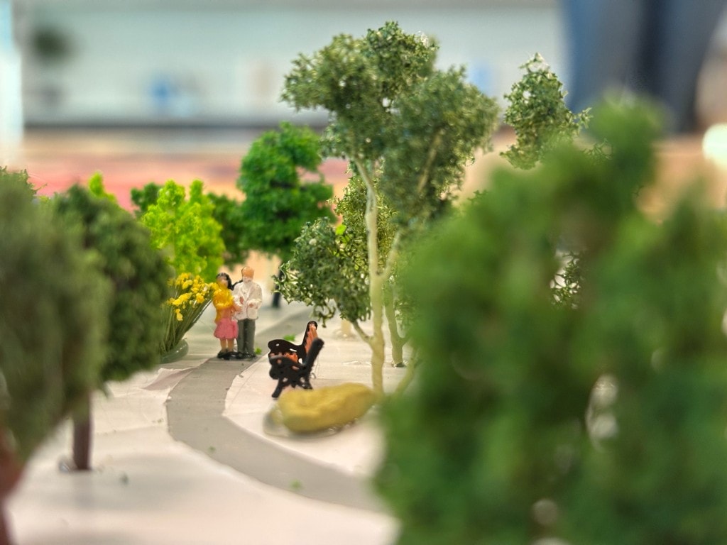 Close-up of the physical diorama showing miniature trees, paths, and figures in the landscape.