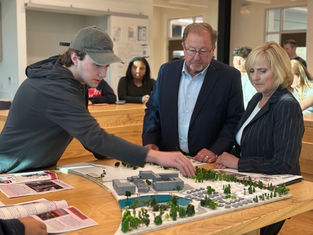 Design team and reviewers gathered around the physical community model on a work table.